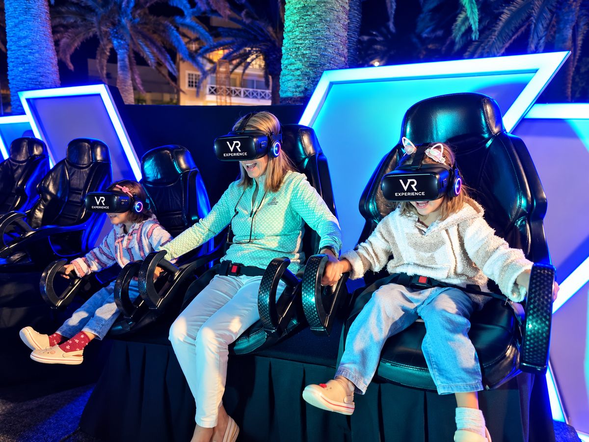 Una abuela y sus dos nietas con visores de VR Experience, tomadas de la mano en las butacas